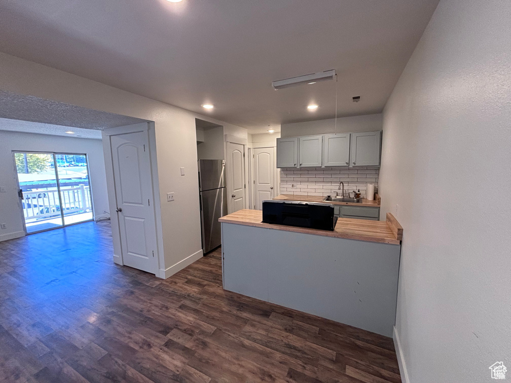 Kitchen with freestanding refrigerator, a peninsula, decorative backsplash, dark wood-type flooring, and gray cabinets