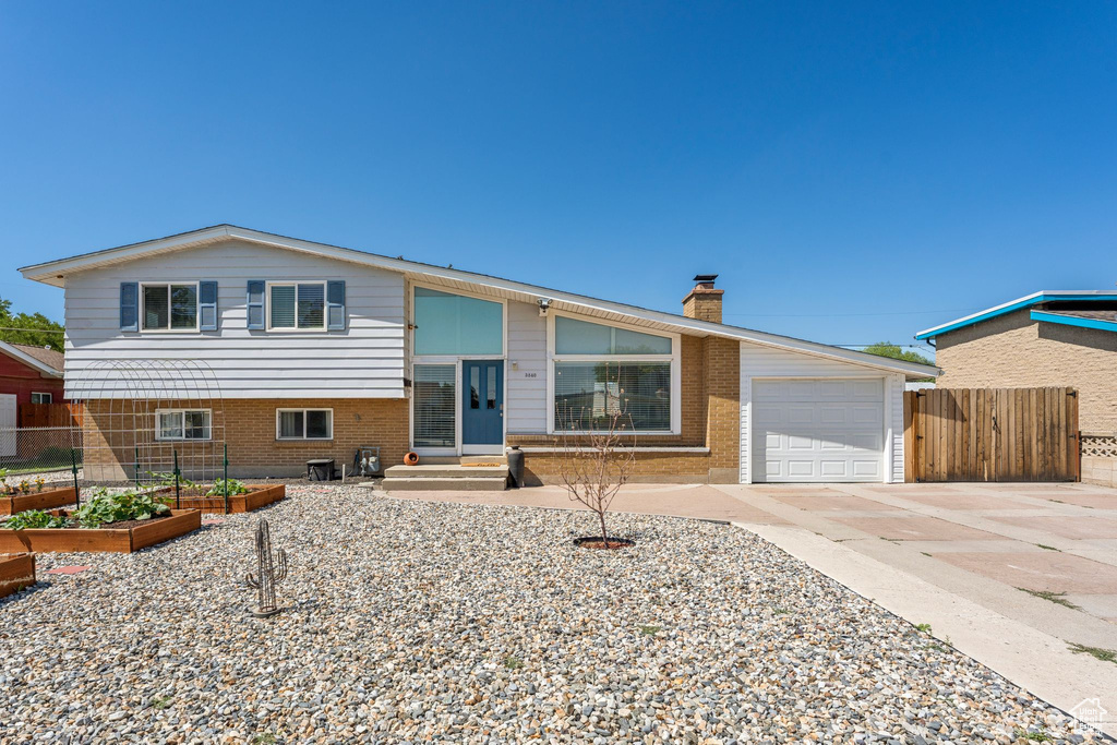 Tri-level home with a garden, an attached garage, driveway, a chimney, and entry steps