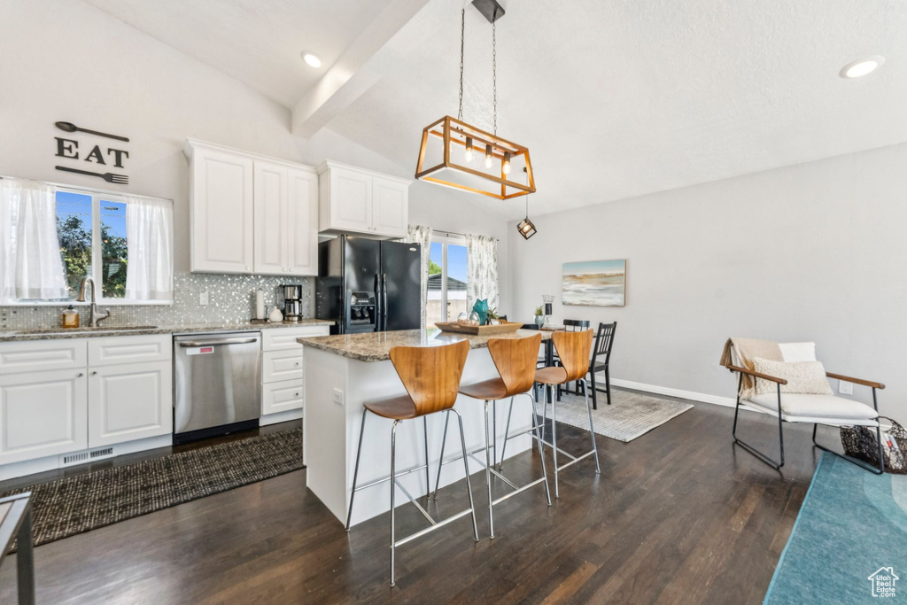 Kitchen featuring stainless steel dishwasher, black fridge, a breakfast bar, dark wood-style floors, and light stone counters