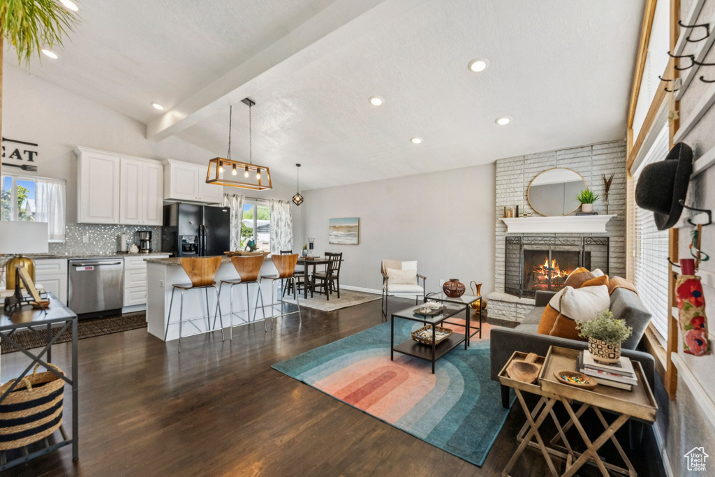 Living area with recessed lighting, dark wood-style flooring, a brick fireplace, and beam ceiling