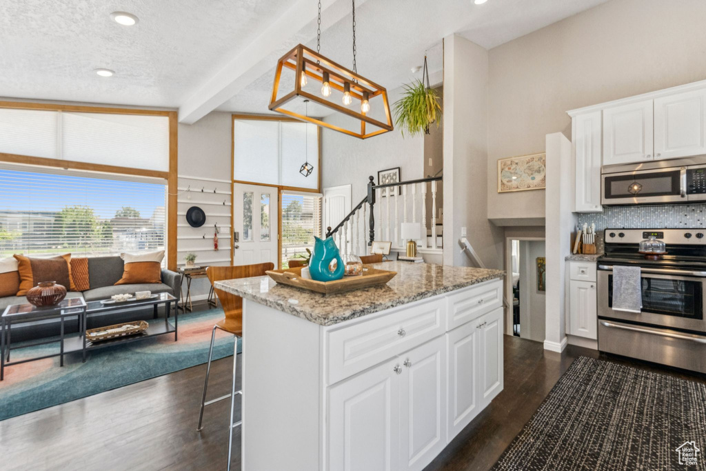Kitchen featuring appliances with stainless steel finishes, beamed ceiling, dark wood-style floors, a breakfast bar, and open floor plan