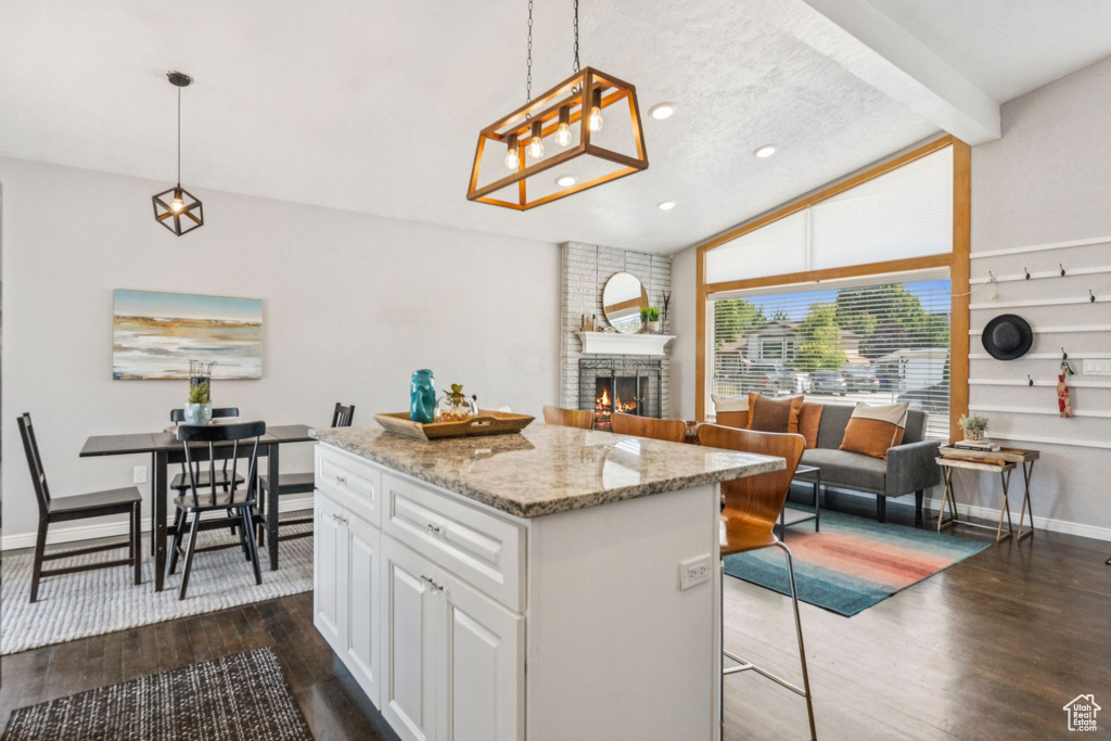 Kitchen featuring dark wood-type flooring, a large fireplace, a center island, open floor plan, and white cabinets