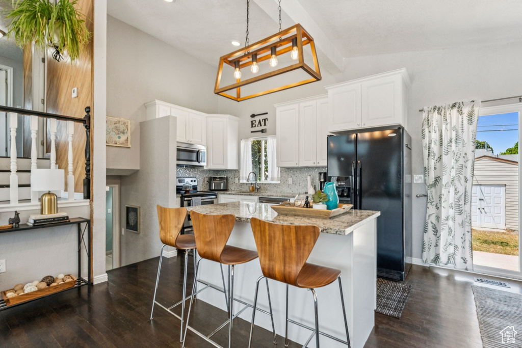 Kitchen featuring appliances with stainless steel finishes, dark wood-type flooring, white cabinetry, tasteful backsplash, and a center island