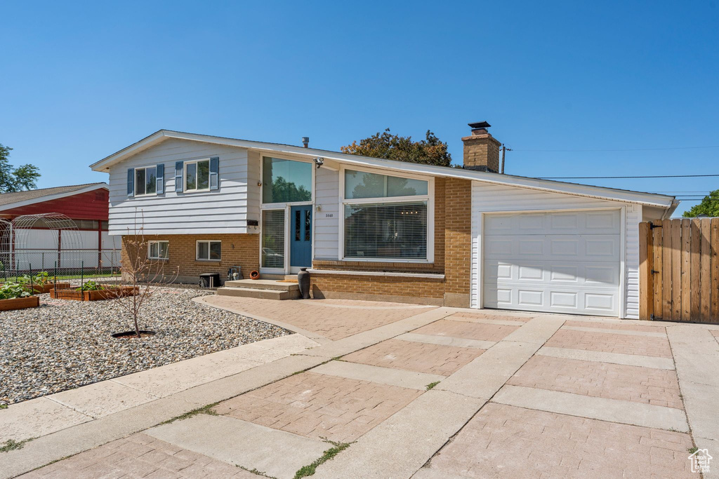 Split level home featuring concrete driveway, brick siding, a chimney, and a garage