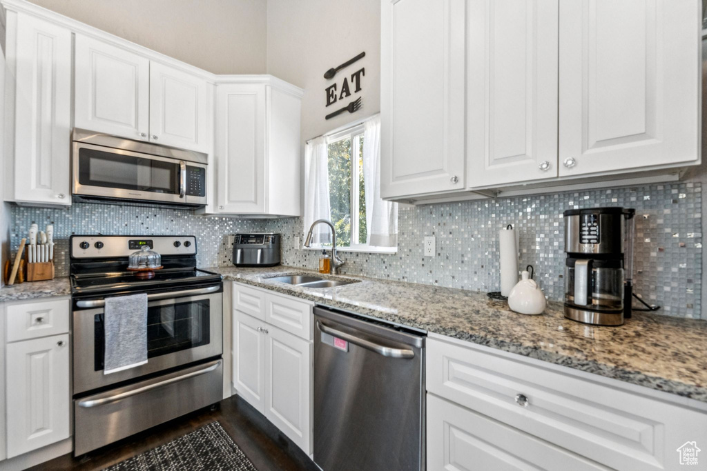 Kitchen featuring stainless steel appliances, white cabinetry, tasteful backsplash, and light stone countertops