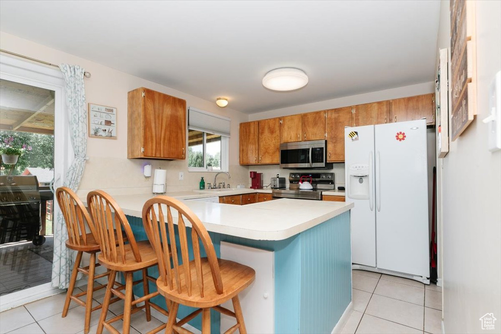 Kitchen featuring stainless steel appliances, light tile patterned floors, brown cabinets, a peninsula, and light countertops