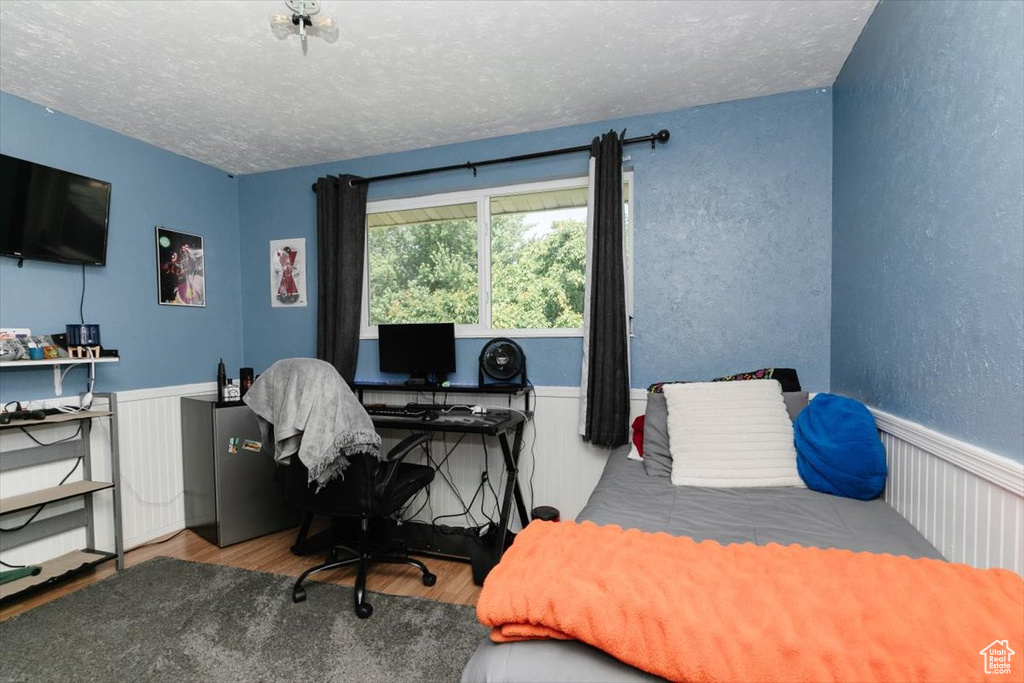 Bedroom featuring wood finished floors, a textured ceiling, an office area, a textured wall, and wainscoting