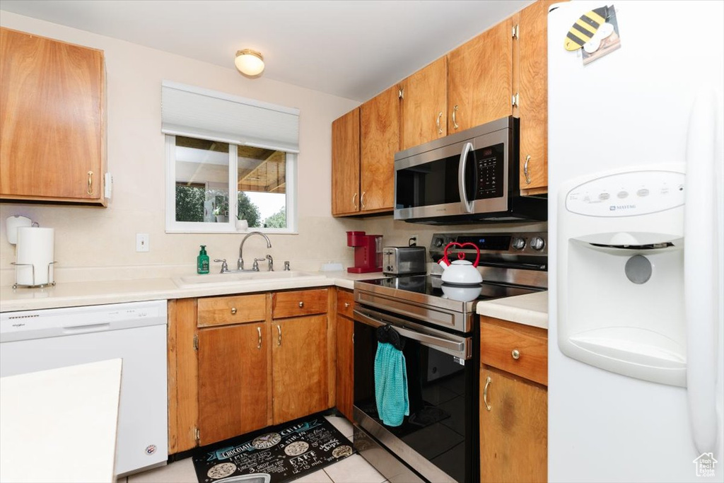 Kitchen with stainless steel appliances, brown cabinetry, light countertops, and light tile patterned floors