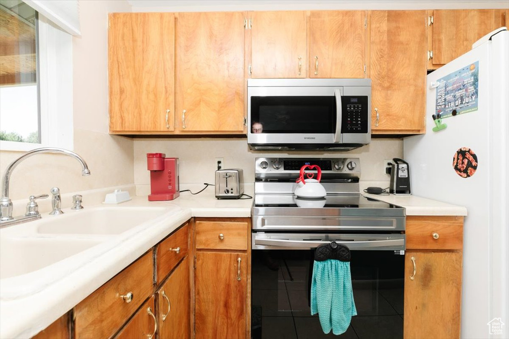 Kitchen with stainless steel appliances, light countertops, brown cabinetry, and tile patterned flooring