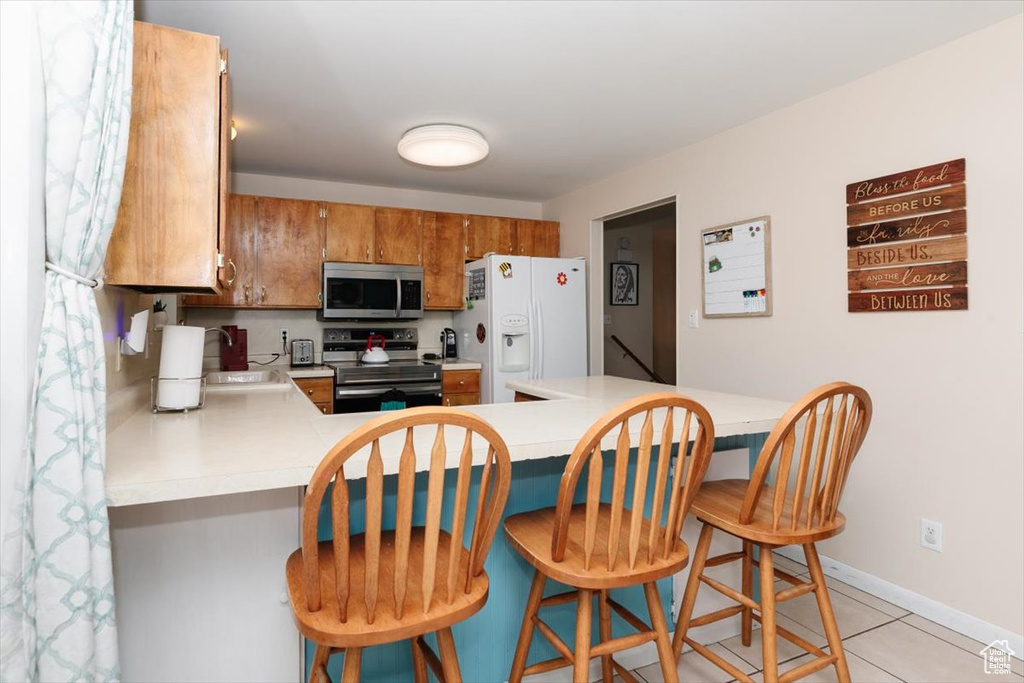 Kitchen with electric stove, stainless steel microwave, white refrigerator with ice dispenser, light countertops, and brown cabinets