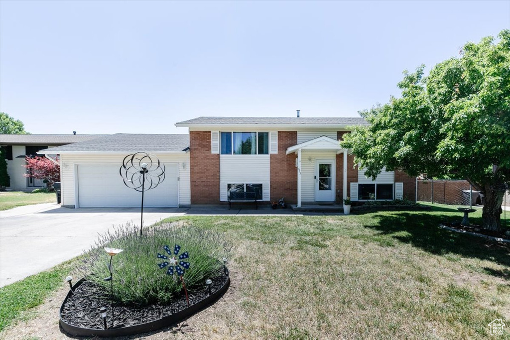 Bi-level home with driveway, a garage, a front lawn, and brick siding
