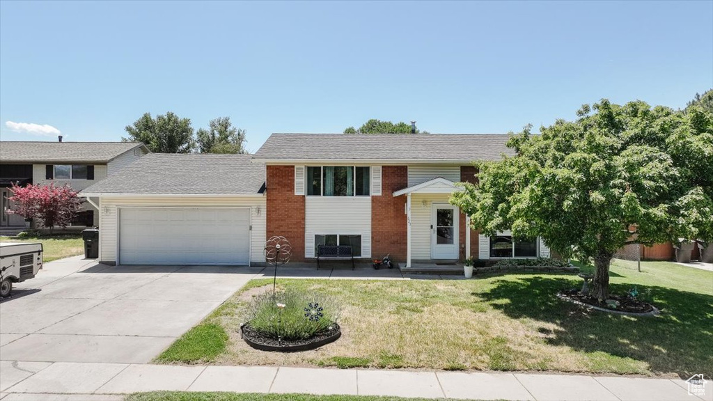 Raised ranch featuring an attached garage, concrete driveway, a front yard, and brick siding