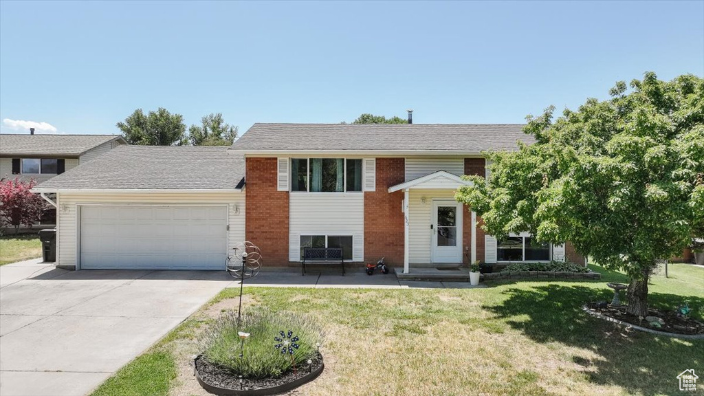 Split foyer home featuring a garage, concrete driveway, and a front lawn