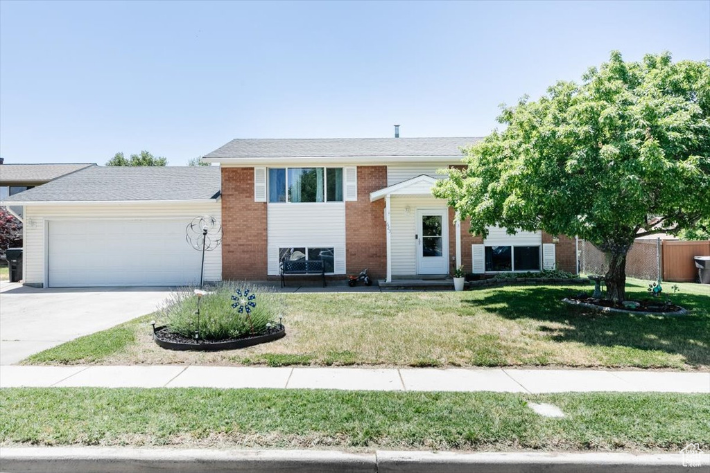 Bi-level home featuring a garage, a front yard, driveway, and brick siding