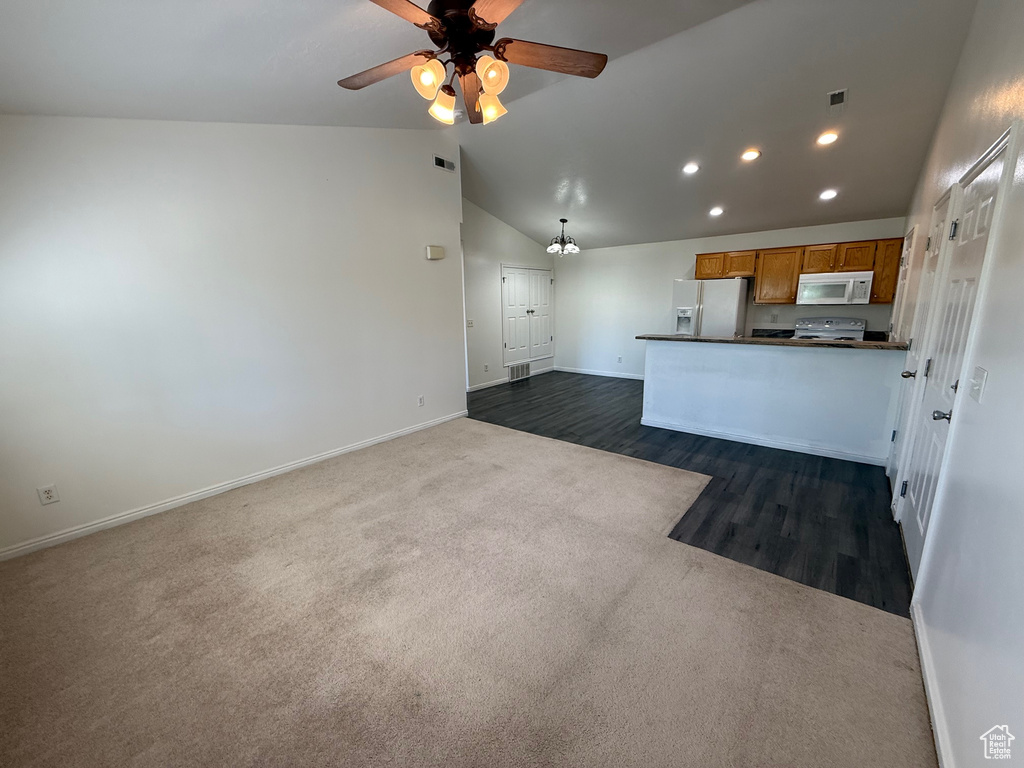 Kitchen with white appliances, dark countertops, vaulted ceiling, dark colored carpet, and brown cabinetry