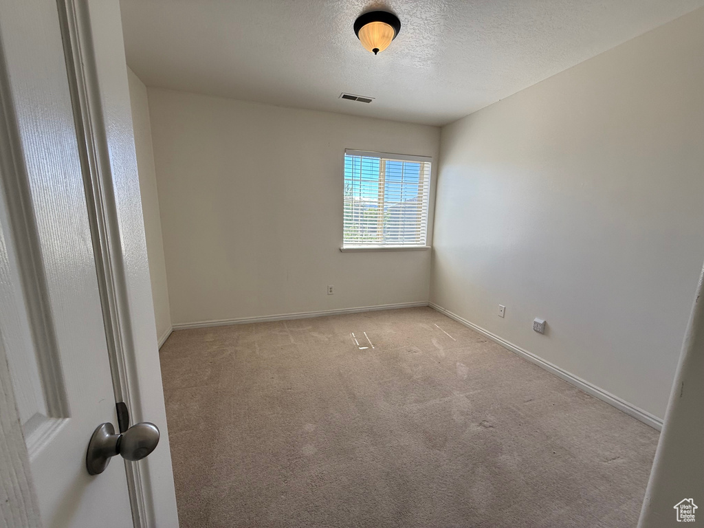 Empty room with light carpet and a textured ceiling