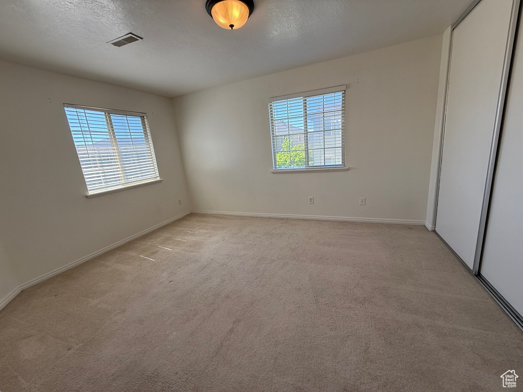 Unfurnished bedroom featuring light carpet, a closet, and a textured ceiling