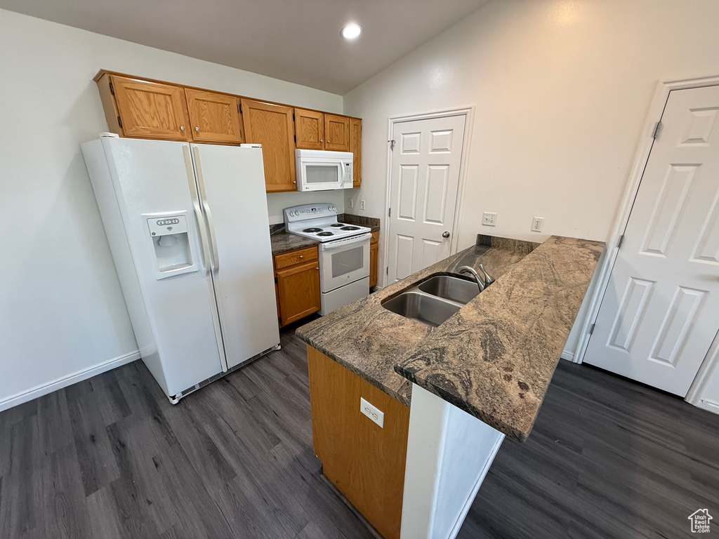 Kitchen featuring white appliances, vaulted ceiling, a peninsula, dark wood-style flooring, and brown cabinets