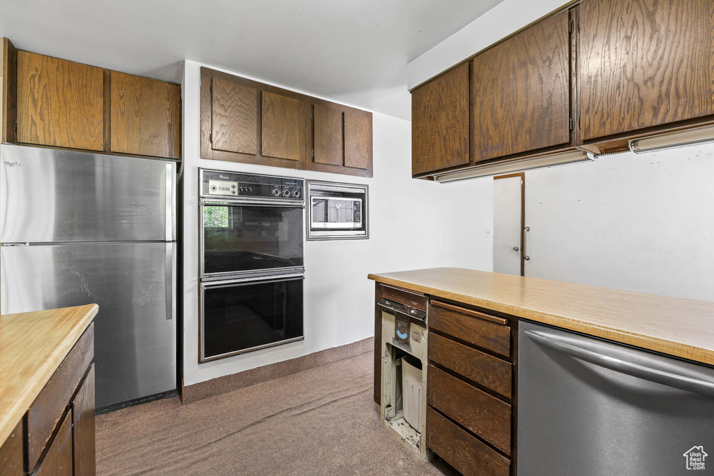 Kitchen with appliances with stainless steel finishes, dark carpet, and dark brown cabinets