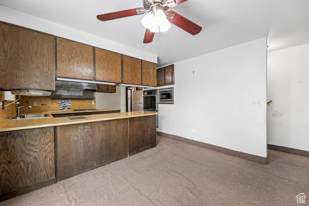 Kitchen featuring dark carpet, stainless steel microwave, ceiling fan, and a peninsula