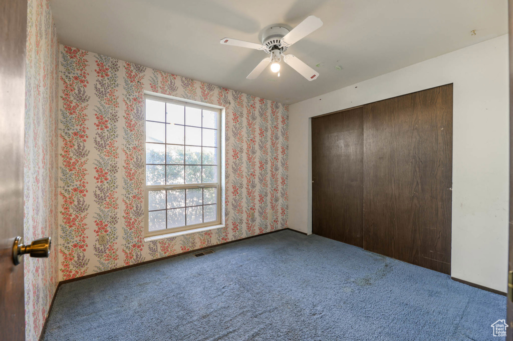 Unfurnished bedroom with carpet, a closet, a ceiling fan, and wallpapered walls