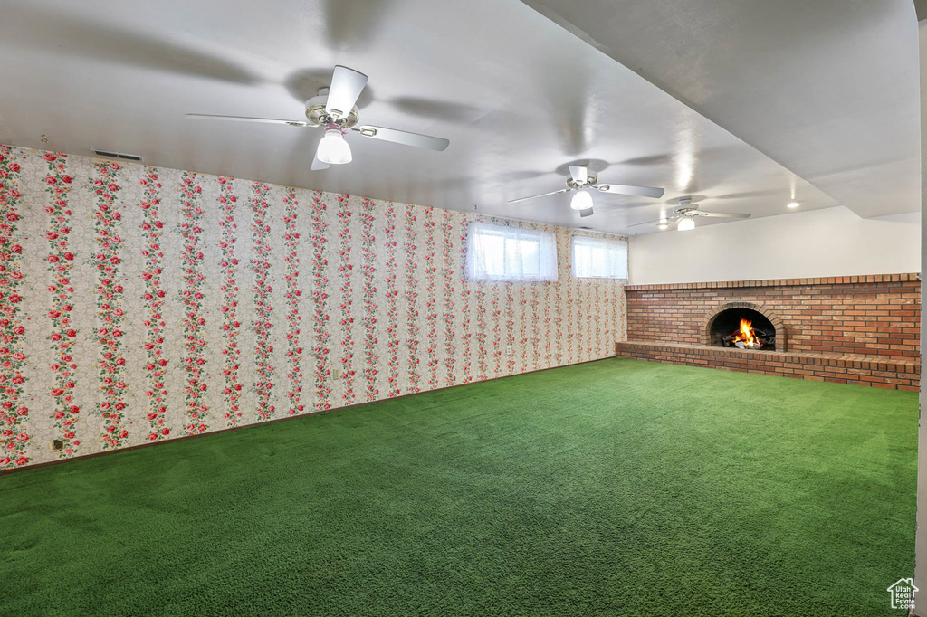 Unfurnished living room featuring a ceiling fan, a brick fireplace, carpet floors, and wallpapered walls