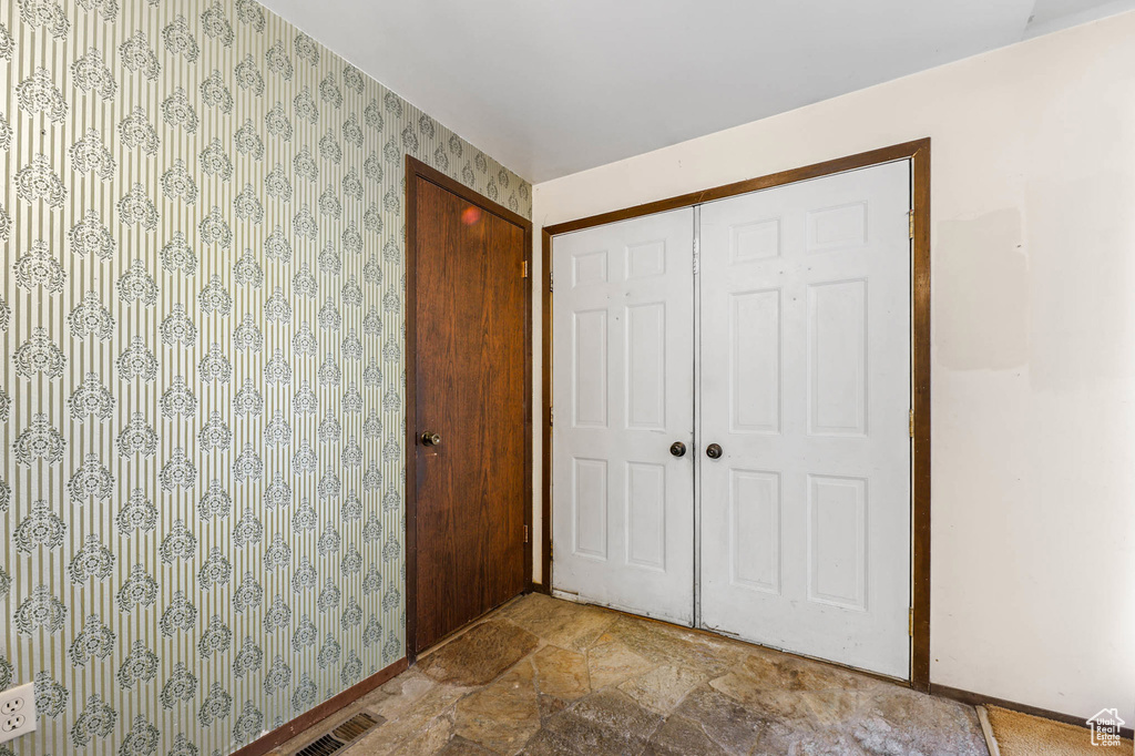 Unfurnished bedroom with wallpapered walls, a closet, and stone finish flooring