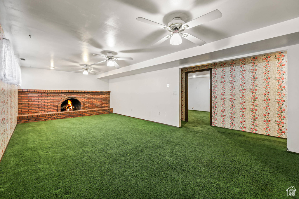 Unfurnished living room featuring a fireplace, carpet, ceiling fan, and brick wall