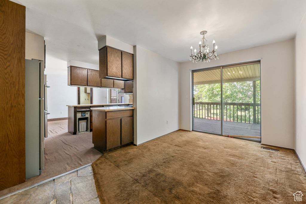 Kitchen with light carpet, a chandelier, freestanding refrigerator, light countertops, and hanging light fixtures