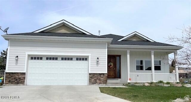 View of front of property featuring stone siding, covered porch, driveway, and an attached garage