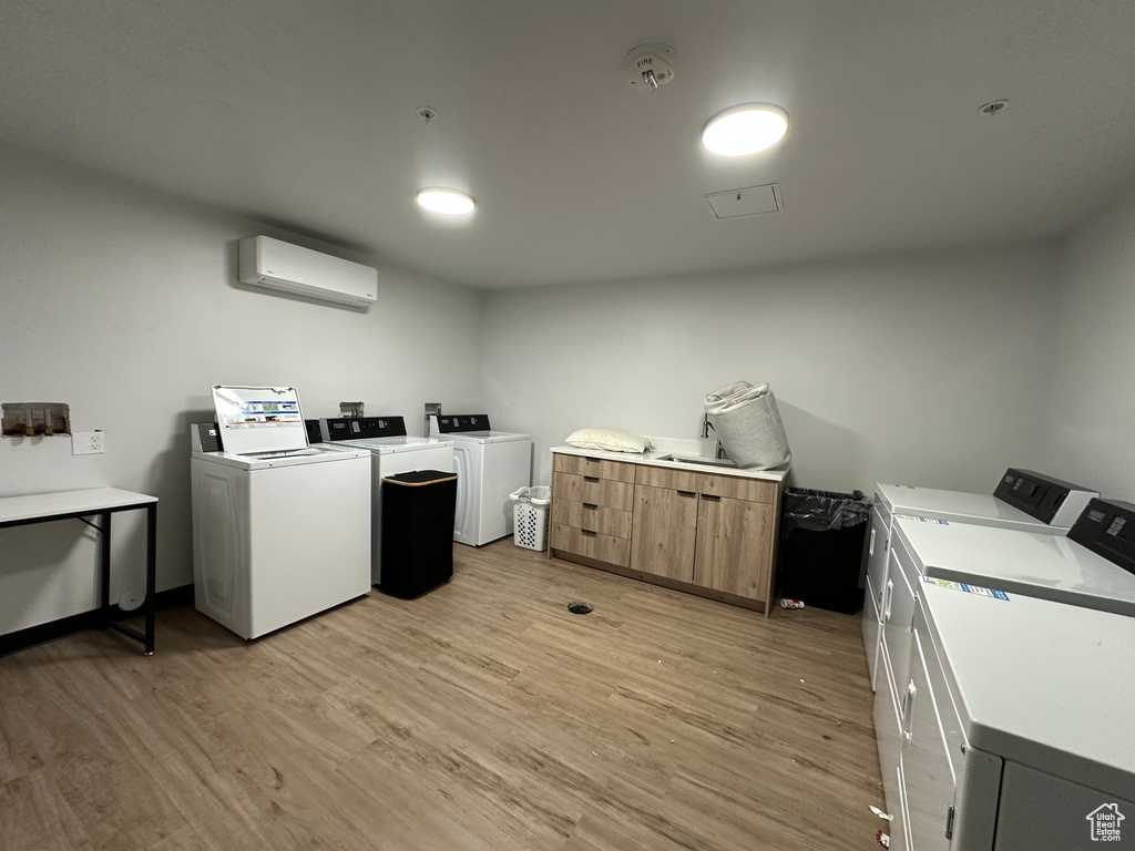 Community laundry with separate washer and dryer, an AC wall unit, and light wood-type flooring