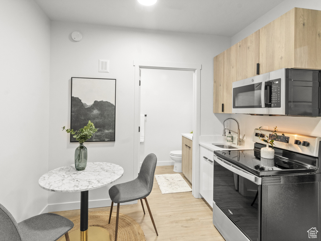 Kitchen featuring appliances with stainless steel finishes, light brown cabinetry, light wood-style flooring, and light countertops