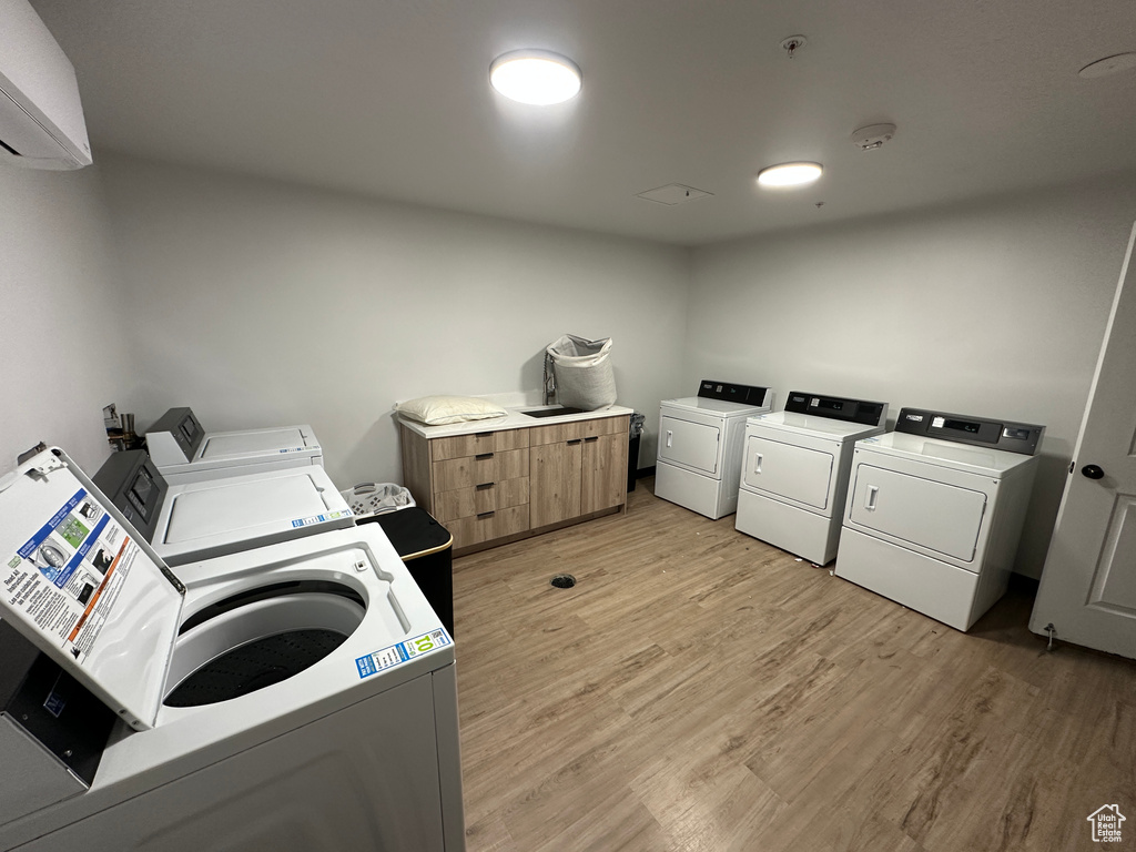 Shared laundry room with washer and dryer, light wood finished floors, and an AC wall unit