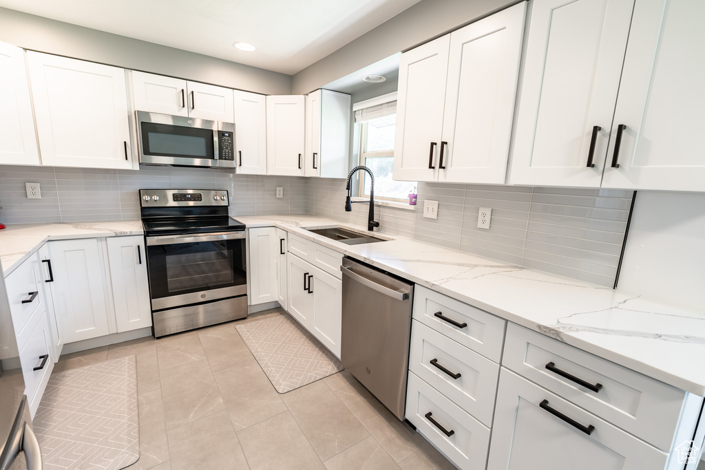 Kitchen featuring appliances with stainless steel finishes, white cabinets, decorative backsplash, light stone countertops, and recessed lighting
