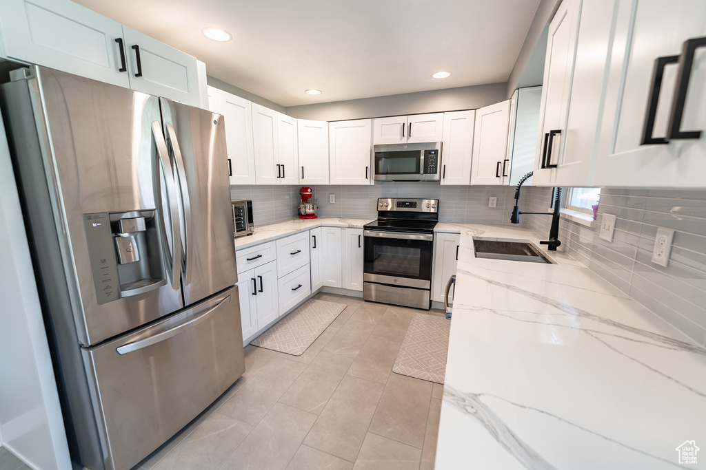 Kitchen featuring stainless steel appliances, backsplash, white cabinetry, light stone countertops, and recessed lighting