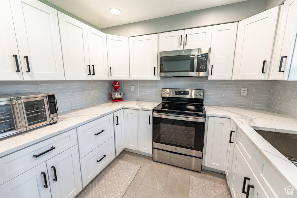 Kitchen with appliances with stainless steel finishes, white cabinets, light tile patterned floors, tasteful backsplash, and light stone counters