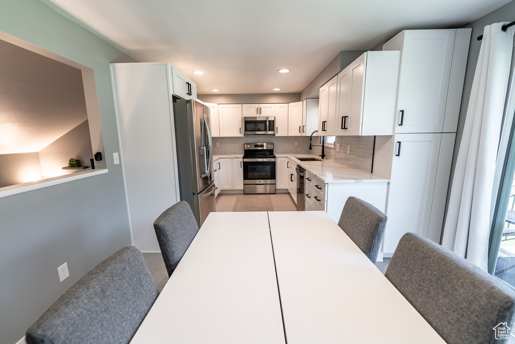 Kitchen featuring appliances with stainless steel finishes, backsplash, light countertops, white cabinets, and recessed lighting