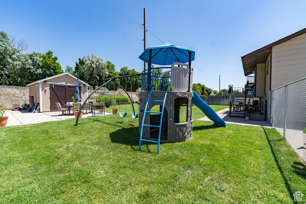 View of playground featuring a fenced backyard, a patio, and a storage unit