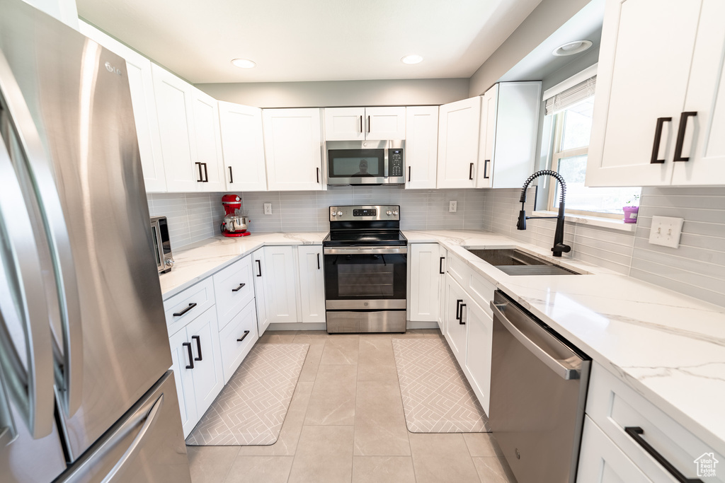 Kitchen featuring stainless steel appliances, white cabinetry, tasteful backsplash, light stone countertops, and recessed lighting
