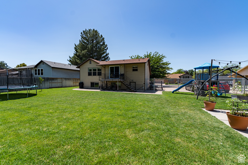 Back of house with a playground, a trampoline, a fenced backyard, a patio area, and stairs