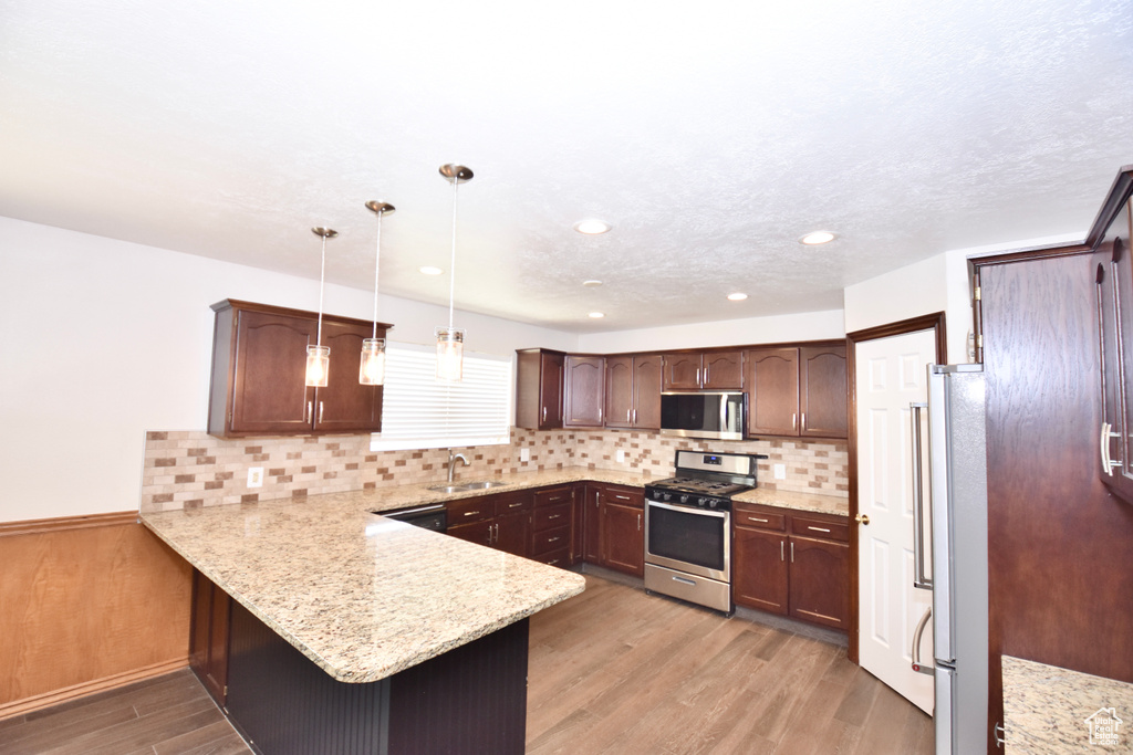 Kitchen featuring appliances with stainless steel finishes, a peninsula, light wood-style floors, dark brown cabinets, and tasteful backsplash