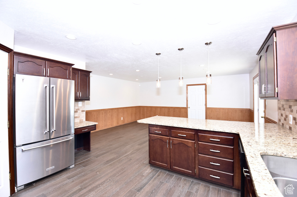 Kitchen featuring high end fridge, wainscoting, a peninsula, wood finished floors, and light stone countertops