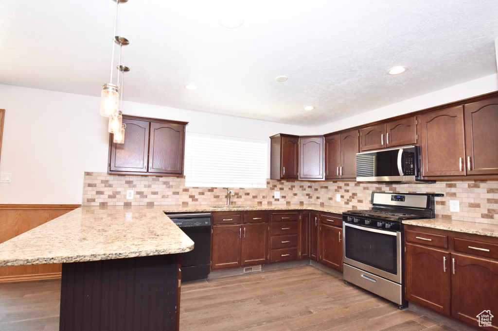 Kitchen featuring appliances with stainless steel finishes, a peninsula, light wood finished floors, decorative backsplash, and dark brown cabinets