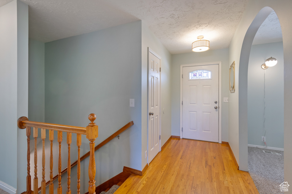 Foyer entrance with a textured ceiling, arched walkways, and wood finished floors