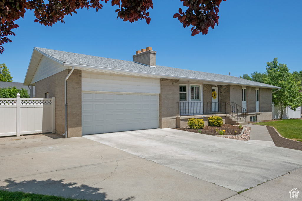 Ranch-style home featuring brick siding, a garage, a chimney, and driveway