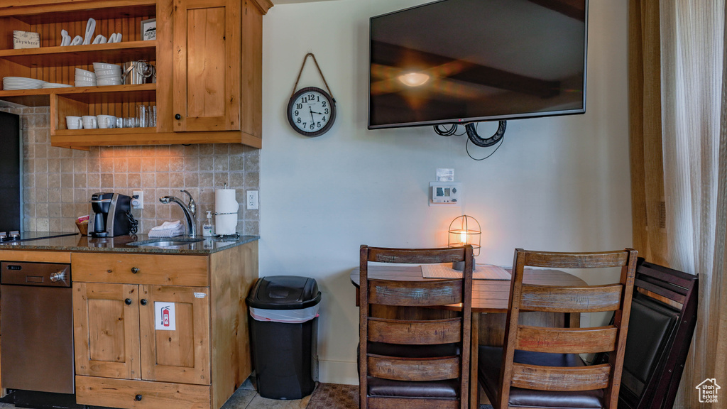 Kitchen with dishwasher, dark stone counters, and backsplash