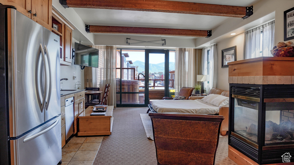 Bedroom with freestanding refrigerator, beam ceiling, a tiled fireplace, access to exterior, and light carpet