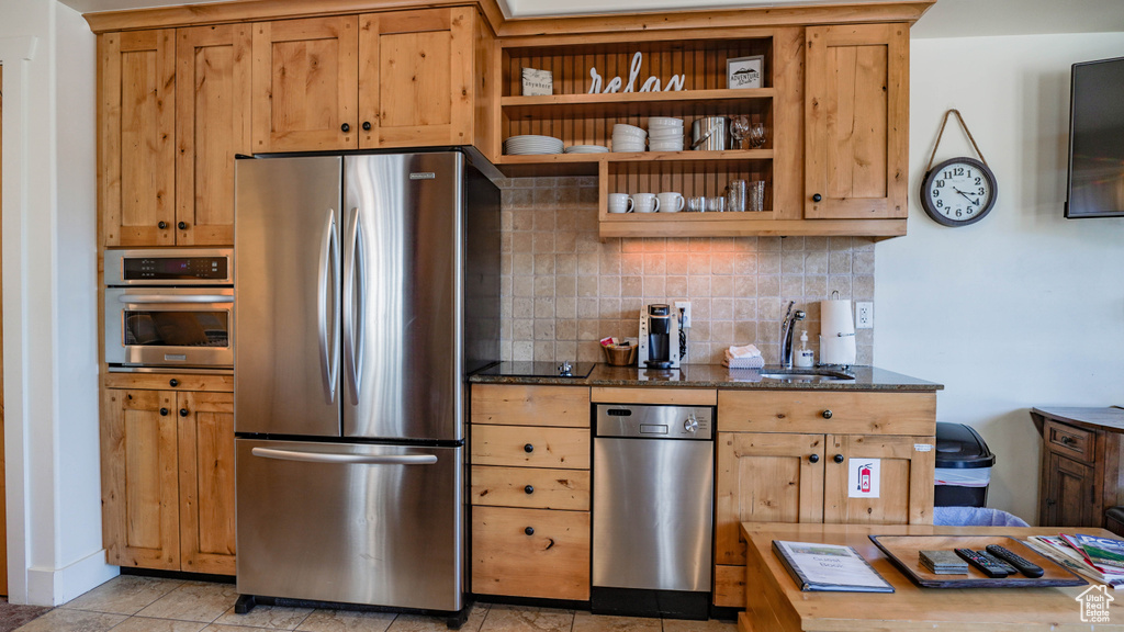 Kitchen with appliances with stainless steel finishes, decorative backsplash, dark stone counters, open shelves, and light tile patterned flooring