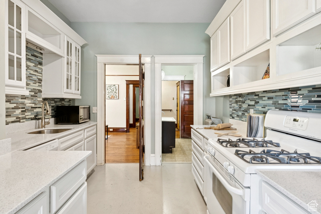 Kitchen with white range with gas stovetop, open shelves, tasteful backsplash, and white cabinetry