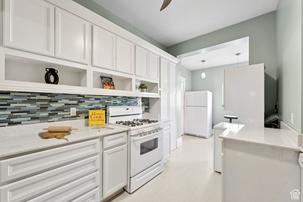 Kitchen with white appliances, open shelves, tasteful backsplash, white cabinetry, and light stone counters